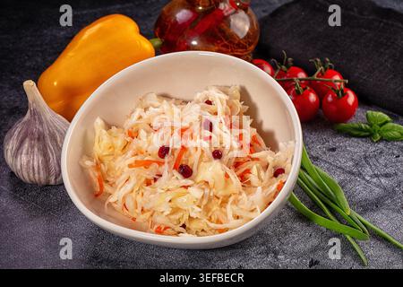 Homemade fermented cabbage salad, sauerkraut, with carrot cranberry in rustic bowl. Still life with fresh vegetables like pepper, garlic, tomato on da Stock Photo
