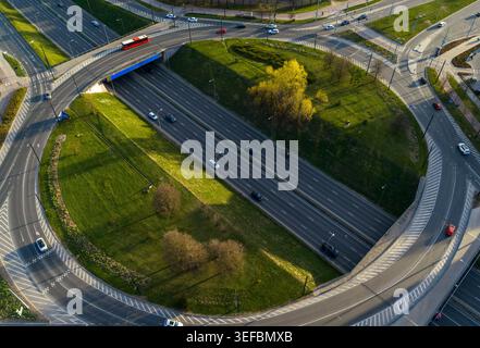 Aerial view of a multi-level highway interchange with traffic and a red bus driving on asphalt roads surrounded by green grass and trees in Vilnius Co Stock Photo