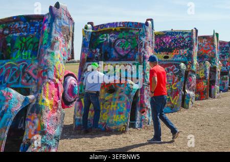 A man spray paints graffiti on a car at the Cadillac Ranch Route 66 in Amarillo Texas USA Stock Photo