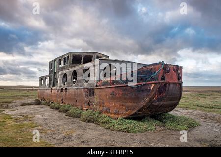 Weathered shipwreck of a wooden boat resting on the tidal salt marsh flat at Blakeney, Norfolk, England Stock Photo