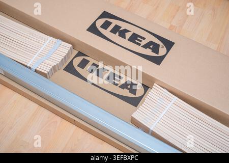 Prague, CZ -21.05.2023: wooden slats and a steel rail rest on IKEA branded cardboard packaging during home assembly. The flat pack components represen Stock Photo