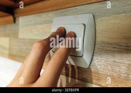 Human hand with two fingers pressing a white dual light switch on a modern wood paneled wall, controlling power and lighting in a contemporary interio Stock Photo