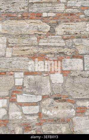 Large, uneven blocks of grey and tan natural stone are integrated with rows of traditional red bricks. The rustic facade features visible mortar joint Stock Photo