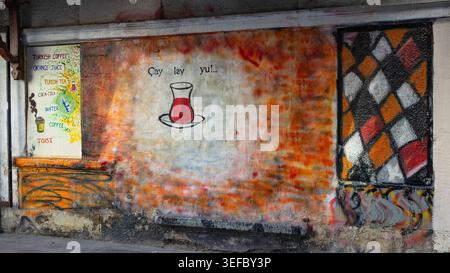 Colorful street art featuring a traditional Turkish tea glass and a hand-painted beverage menu on a textured, rustic urban wall Stock Photo