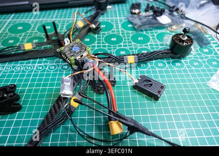 partially assembled FPV racing drone on a green cutting mat, carbon fiber frame with motors, electronic components, wiring, and small hardware pieces Stock Photo
