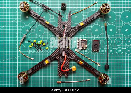partially assembled FPV racing drone on a green cutting mat, carbon fiber frame with motors, electronic components, wiring, and small hardware pieces Stock Photo