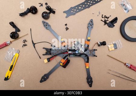 A disassembled FPV drone  a carbon fiber frame, flight controller, ESC electronic speed controler , motors,. Various tools and small components are sc Stock Photo