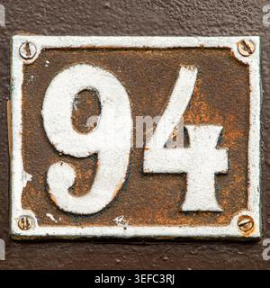 Close-up of rusty vintage metal house number 94 with textured surface and distressed industrial appearance. Stock Photo