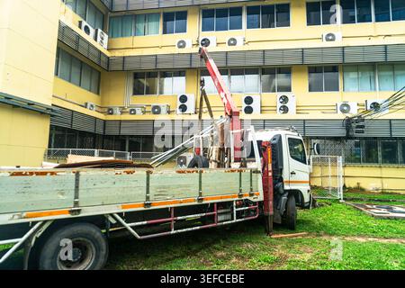 A construction scene showing a crane mounted on a flatbed truck lifting and installing structural elements outside a multi-story building with multipl Stock Photo