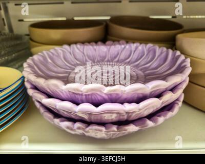 Three beautiful lavender ceramic plates, intricately designed to resemble sunflower petals, are neatly stacked on a white shelf Stock Photo