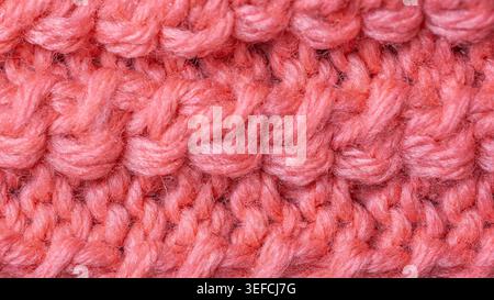 Detailed view of a soft, fuzzy coral pink yarn knitted into a complex pattern, showcasing the texture and depth of the material Stock Photo