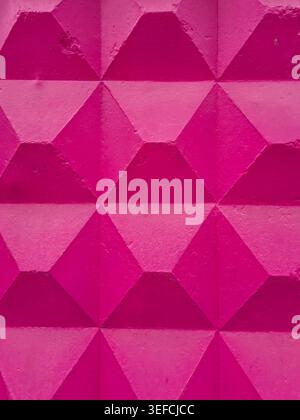 A close-up view of a textured concrete surface painted in a bright, bold pink, showcasing a repeating pattern of geometric diamond shapes Stock Photo