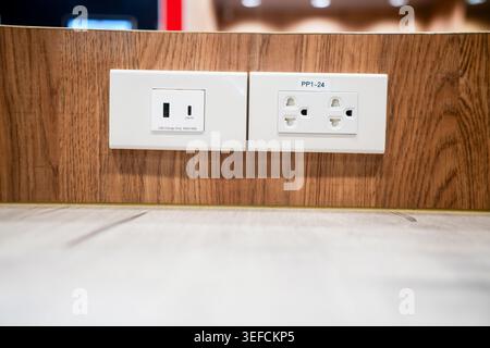 Close-up image of two electrical outlets mounted on a wooden wall near the floor, showing a power connection point with a clean and modern appearance. Stock Photo