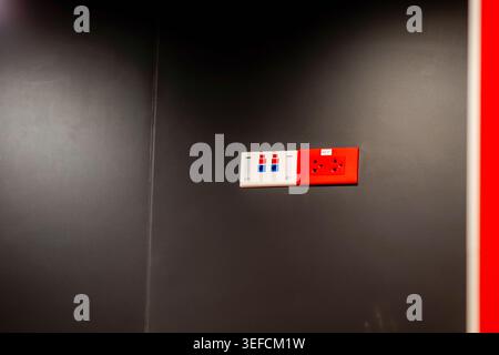 This image features a set of power outlets mounted on a sleek, modern black wall, including a red electrical socket and white switch panel, highlighti Stock Photo