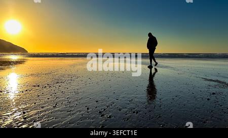 Golden Hour Horizon: Silhouette of a Solitary Man Walking on a Coastal Beach in Northern Spain as a Life Journey Metaphor. Stock Photo