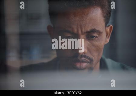 Black Man Working on Laptop through Window in Remote Work Setting Stock Photo