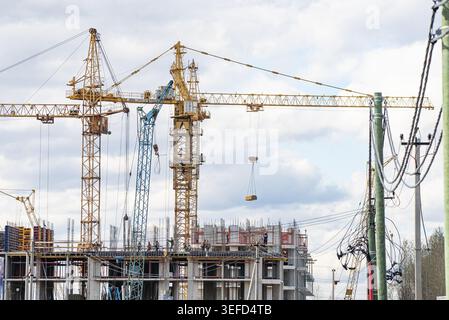 Tower cranes working at a busy construction site, lifting materials and actively building a new multi-story residential or commercial building for urban development and city expansion Stock Photo