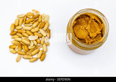 Many roasted peanuts and a jar of peanut butter on white background Stock Photo
