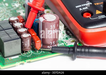 Close-up of a circuit board with electronic components and a multimeter with test probes. Concept of electronics diagnostics, electrical testing, repa Stock Photo