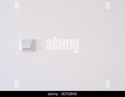 A white double rocker light switch is installed on a plain painted white wall Stock Photo