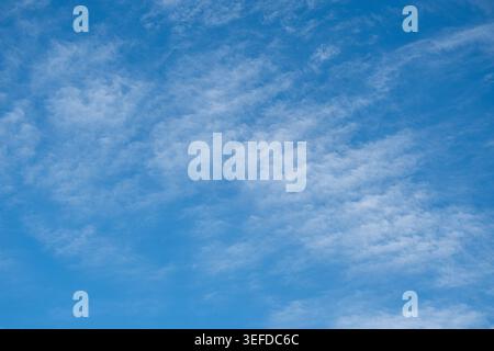 Scattered wispy white clouds drift across a vibrant, bright blue sky during a clear, sunny day. Stock Photo