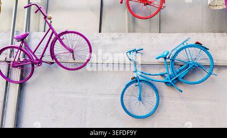Bright painted bicycles mounted on a wall forming a colorful outdoor art installation in the city. The creative urban scene illustrates street culture Stock Photo