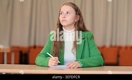 A young student sits alone at a desk and writes notes with calm focus, captured in a balanced frontal shot with shallow depth of field. This scene Stock Photo