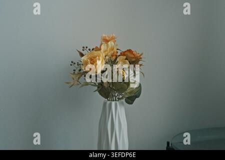 Peach and orange roses in a white geometric vase against a soft grey background indoors. Stock Photo