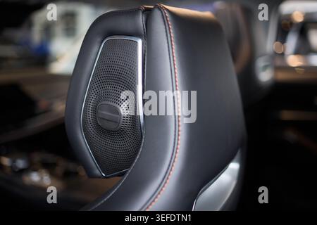 Closeup leather car headrest speaker with red contrast stitching, mesh grille, soft ambient lighting, high-end craftsmanship, tactile texture, modern Stock Photo