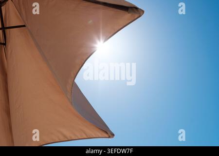 A large umbrella provides shade as bright sunlight shines from behind it on a sunny day, creating a serene outdoor atmosphere. Stock Photo