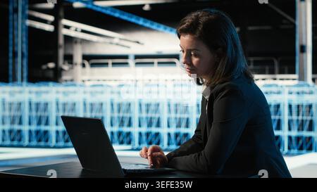 Optimizing server, laptop and software developer in data center doing load balancing. Adjusting system parameters, notebook and woman in server farm at desk improving efficiency Stock Photo