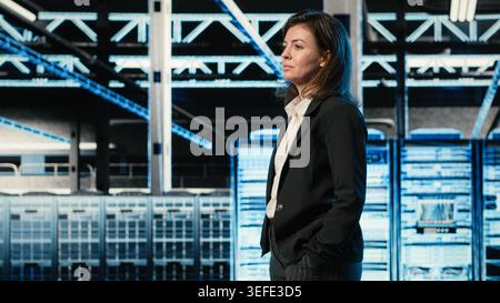 Cheerful data center system administrator takes virtual tour using AR tech, satisfied by rigs performance. Upbeat admin walks in server room with VFX overlay augmented reality simulation Stock Photo