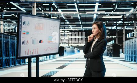 Data center manager looking at infrastructure status infographics on monitor. Server farm employee analyzing AR simulation and audit charts on display to oversee equipment Stock Photo