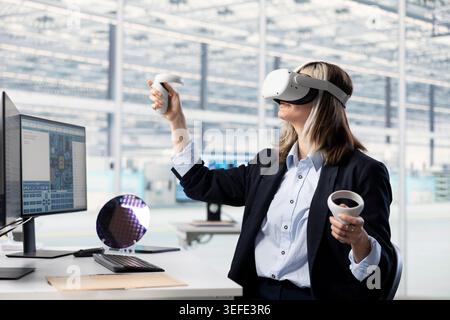 Woman using VR glasses gear to do semiconductors prototyping in office. Female engineer doing technical innovations in microchip factory RD lab using virtual reality simulation Stock Photo