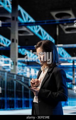 Data center software developer using tablet to inspect infrastructure rackmounts, updating network systems. IT expert using device to ensure stable server room operations, overseeing equipment rigs Stock Photo