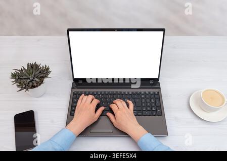 Woman typing on laptop with blank screen mockup in minimalist workspace, top view office setup with smartphone, coffee cup and succulent plant Stock Photo
