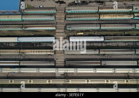 An aerial perspective captures numerous freight trains parked neatly along parallel railway tracks within a large industrial rail yard under clear day Stock Photo