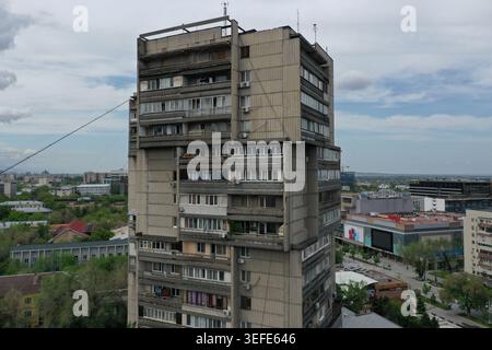 A tall concrete apartment block featuring numerous balconies stands prominently against a backdrop of sprawling urban development and scattered greene Stock Photo