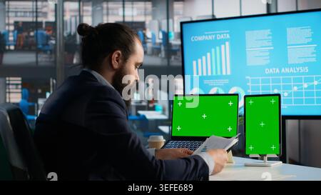 Green screen, tablet and laptop, data analysis on documents, business KPIs for decision making, businessman checking reports. Financial management, insights and metrics, corporation. Stock Photo