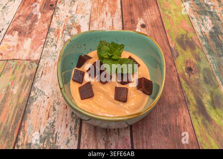 Creamy dessert topped with dark guava paste cubes and fresh mint leaves sits in a turquoise bowl on rustic wood. Stock Photo