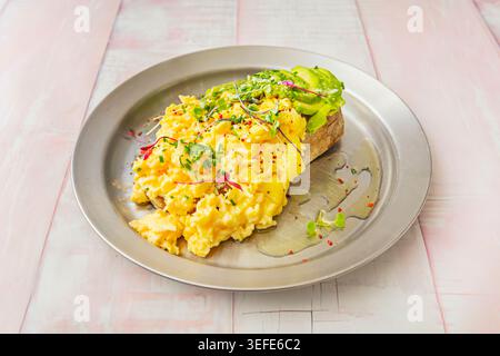 Creamy scrambled eggs and sliced avocado on toast topped with chives and microgreens s Stock Photo