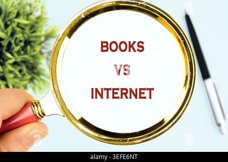 A human hand firmly holds a magnifying glass over a white text clearly displaying Books versus Internet in bold red letters Stock Photo