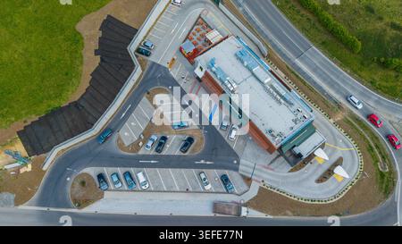 Aerial view of a modern McDonald's fast-food restaurant with a drive-thru lane, parking lot with cars, and people walking near the entrance next to a Stock Photo