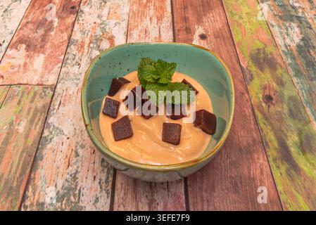 Creamy dessert topped with dark guava paste cubes and fresh mint leaves sits in a turquoise bowl on rustic wood. Stock Photo
