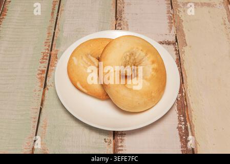 Two golden ring-shaped breads sit stacked on a white plate over a distressed whitewashed wooden surface. Stock Photo