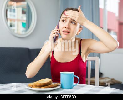 Displeased woman talking on mobile phone while sitting at dinner table Stock Photo
