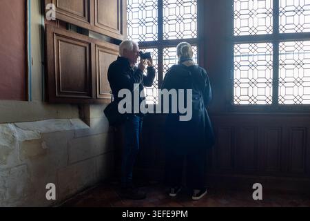 Man holding up a camera to photograph a woman or take a picture out of an ornate, leaded-glass window inside a historical building Stock Photo