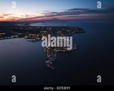 Aerial view of the Island of Ortigia with city lights at dusk and Mount Etna in the distance Syracuse, Sicily, Italy. Stock Photo