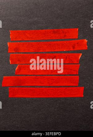 Red stripes of adhesive tape arranged in a row on a dark black textured surface Stock Photo