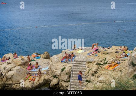 High angle view of people sunbathing on rocky cliffs by clear blue water in Rovinj Croatia Stock Photo